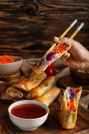 Woman eating tasty fried spring rolls on wooden backgroundの写真素材