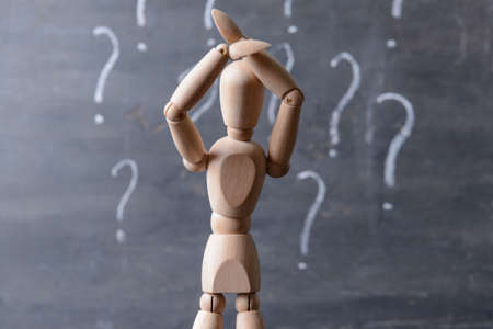 Wooden mannequin with question marks on dark background