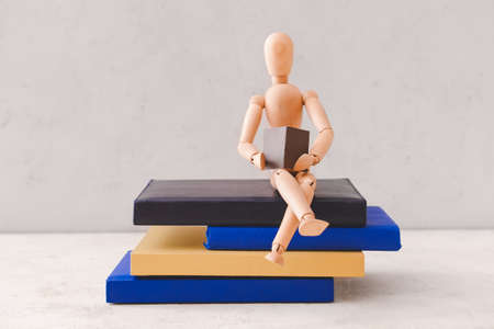 Wooden mannequin with books on light background