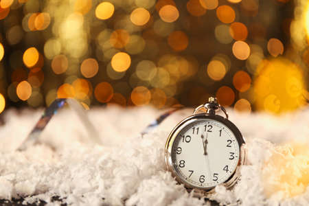 Pocket watch on snow against blurred lights. Christmas time