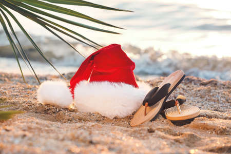 Santa hat, tropical leaf and flip-flops on sea beach. Christmas vacation conceptの写真素材