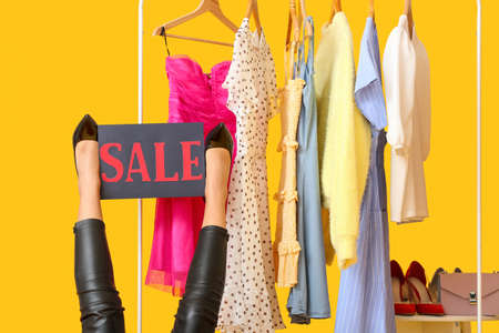 Legs of beautiful young woman and rack with clothes on color background. Black Friday saleの写真素材