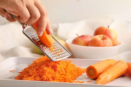 Woman grating carrot on light backgroundの写真素材
