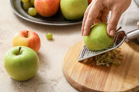 Woman grating apples at tableの写真素材