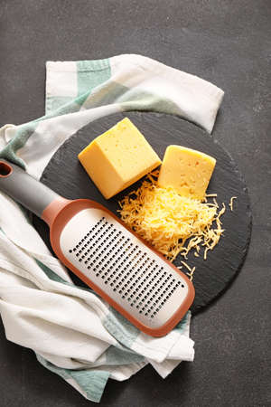 Tasty cheese and grater on dark background