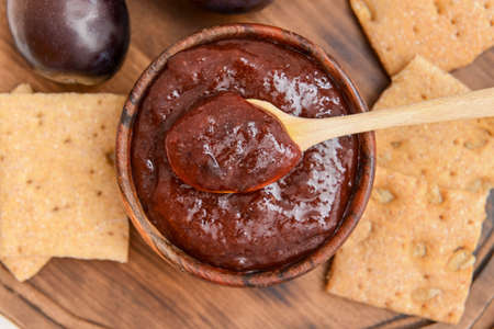 Bowl with delicious homemade plum jam on wooden board
