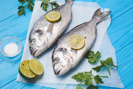 Raw dorado fish with parsley and lime on color wooden background