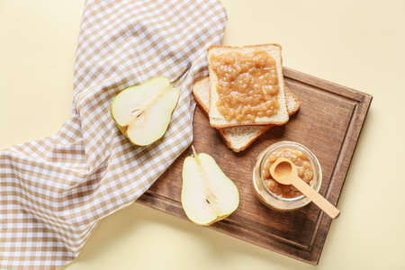 Jar of tasty pear jam with bread on color backgroundの写真素材