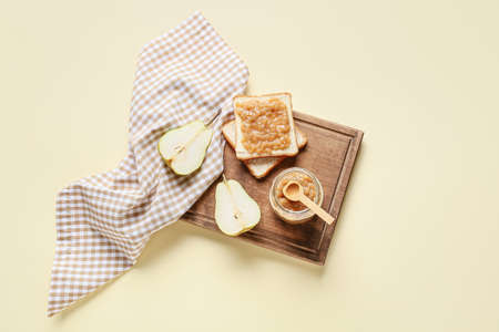 Jar of tasty pear jam with bread on color backgroundの写真素材
