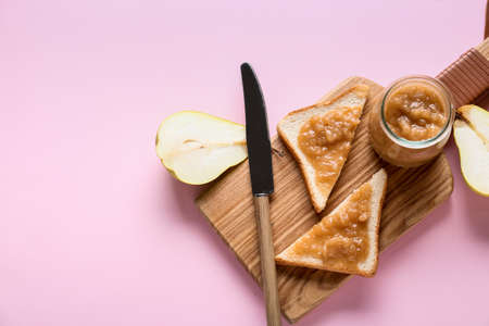 Jar of tasty pear jam with bread on color backgroundの写真素材