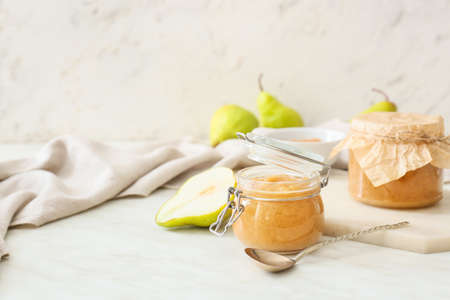 Jar of tasty pear jam on light background