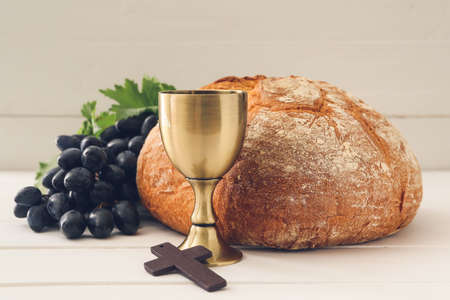 Chalice of wine with bread and cross on white wooden backgroundの写真素材