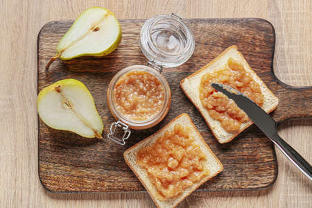 Jar of tasty pear jam with bread on wooden backgroundの写真素材