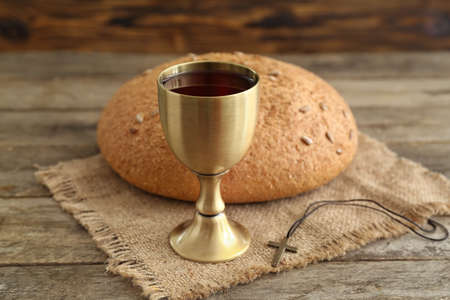 Chalice of wine with bread and cross on wooden background