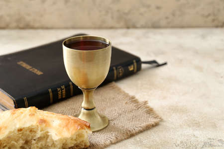 Chalice of wine with bread and Holy Bible on gray background