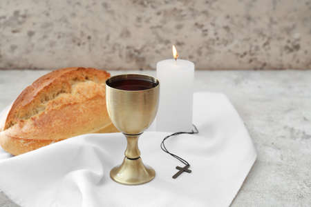 Chalice of wine with bread, cross and candle on gray background