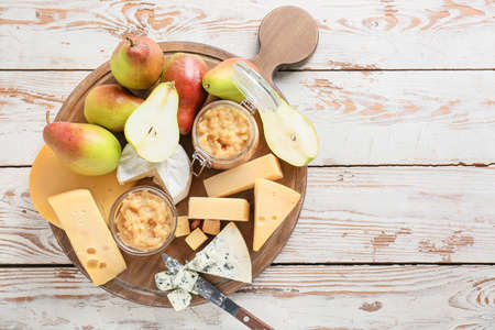 Tasty pear jam with different cheeses on white wooden background