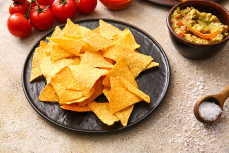 Plate with tasty nachos and guacamole sauce on light background