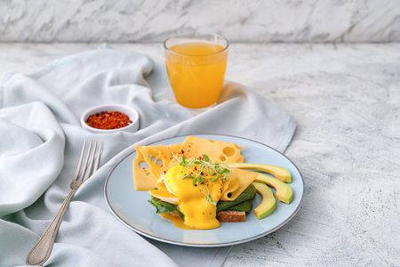 Tasty sandwich with florentine egg, cheese, avocado and juice on light background