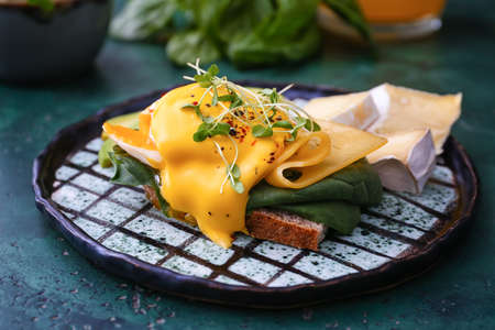 Tasty sandwich with florentine egg, cheese and avocado on color background, closeup