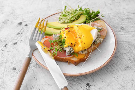 Tasty sandwich with florentine egg, bacon and avocado on light background, closeup