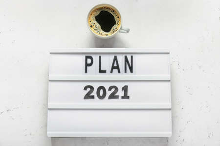 Board with text PLAN 2021 and cup of coffee on light backgroundの写真素材