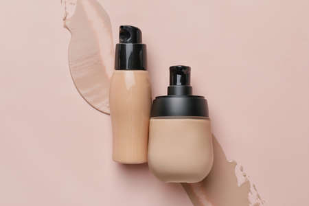 Bottles of makeup foundation and samples on color background