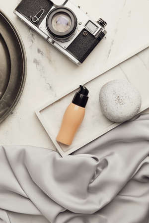 Bottle of makeup foundation and photo camera on light background