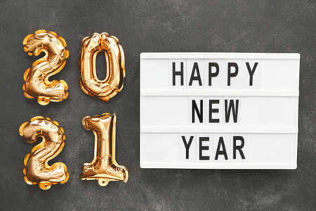 Figure 2020 made of balloons and board with text HAPPY NEW YEAR on dark background