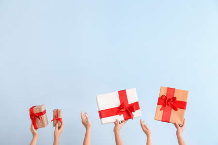 Hands with gift boxes on color background