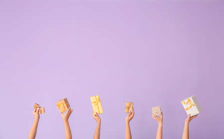 Hands with gift boxes on color backgroundの写真素材