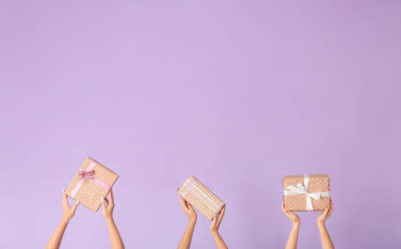 Hands with gift boxes on color background