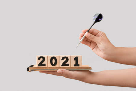 Female hands holding cubes with figure 2021, notebook and dart on light background