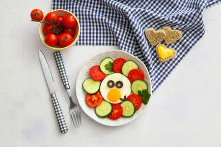 Creative breakfast for children with egg and fresh vegetables on light background