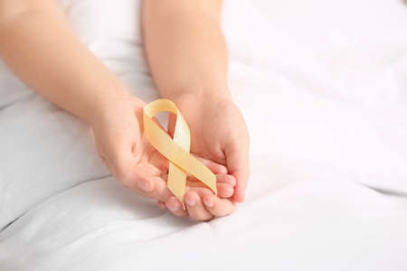Little girl with golden ribbon in clinic, closeup. Childhood cancer awareness concept