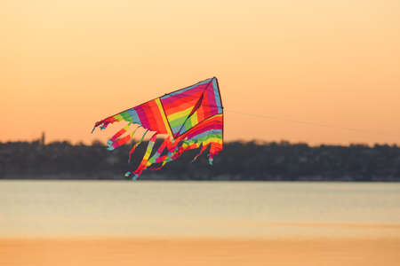 Colorful kite flying near river at sunsetの写真素材