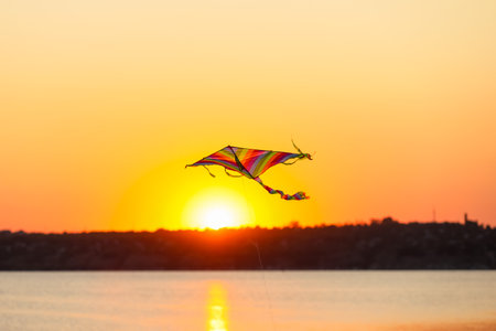 Colorful kite flying near river at sunsetの写真素材