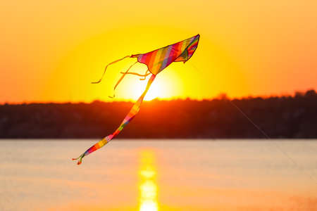 Colorful kite flying near river at sunset
