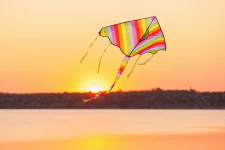 Colorful kite flying near river at sunsetの写真素材