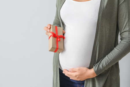 Beautiful pregnant woman with gift on light background, closeupの写真素材