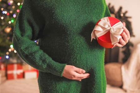 Beautiful pregnant woman with gift at home on Christmas eve, closeupの写真素材