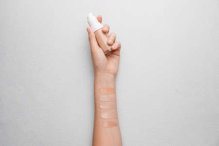Female hand with bottle of makeup foundation and samples on white backgroundの写真素材