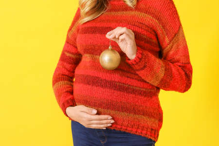 Beautiful pregnant woman with Christmas ball on color backgroundの写真素材