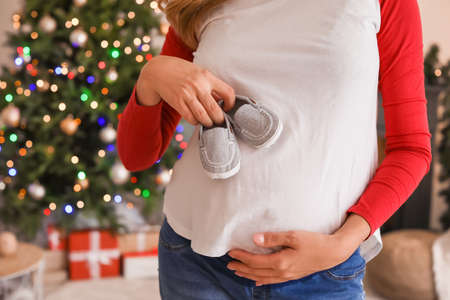 Beautiful pregnant woman with baby shoes at home on Christmas eve, closeup