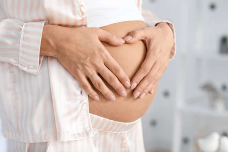 Beautiful pregnant woman making heart with her hands, closeup