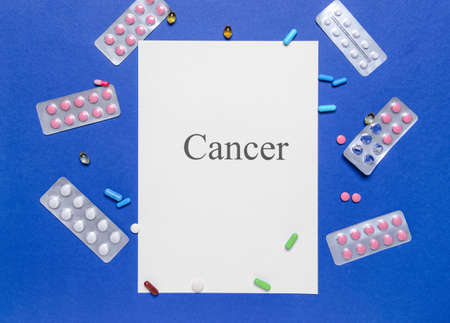 Paper sheet with word CANCER and pills on color backgroundの写真素材