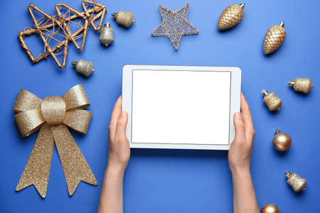 Female hands with tablet computer and Christmas decor on color background