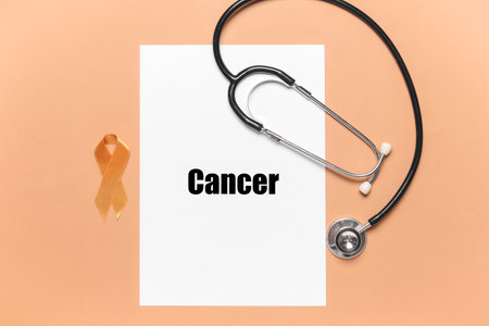 Paper sheet with word CANCER, stethoscope and golden ribbon on color backgroundの写真素材