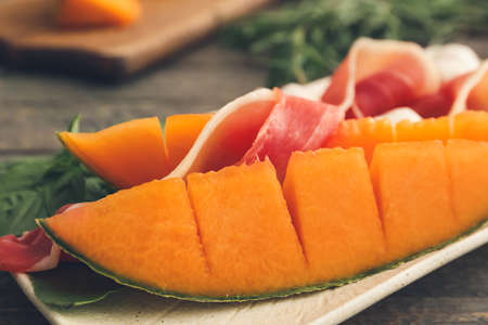 Plate with delicious melon and prosciutto on wooden background, closeupの写真素材