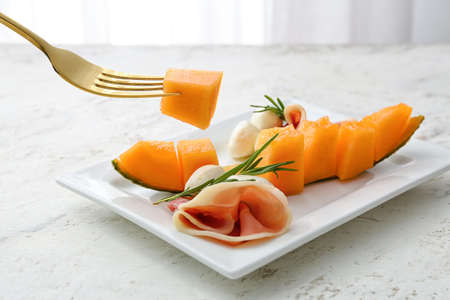 Plate with delicious melon, mozzarella and prosciutto on light tableの写真素材